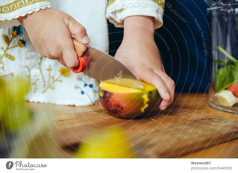 Girl cutting a mango with a children’s knife Mango Mangoes Mango Fruits Mangos kitchen girl females girls Food foods food and drink Nutrition Alimentation