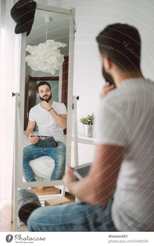 Young man sitting on the bed looking at himself in the mirror home at home beds mirrors eyeing men males view seeing viewing Adults grown-ups grownups adult
