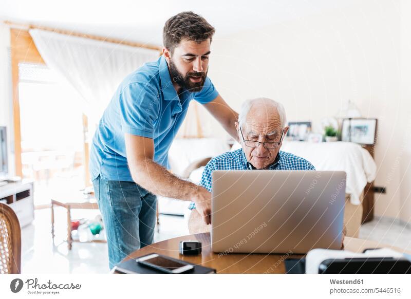 Adult grandson teaching his grandfather to use laptop grandpas granddads grandfathers Laptop Computers laptops notebook senior men senior man elder man