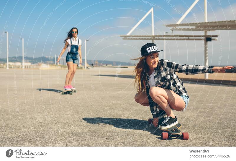 Two young women longboarding on beach promenade woman females female skateboarder female skater female skateboarders skateboarding Adults grown-ups grownups