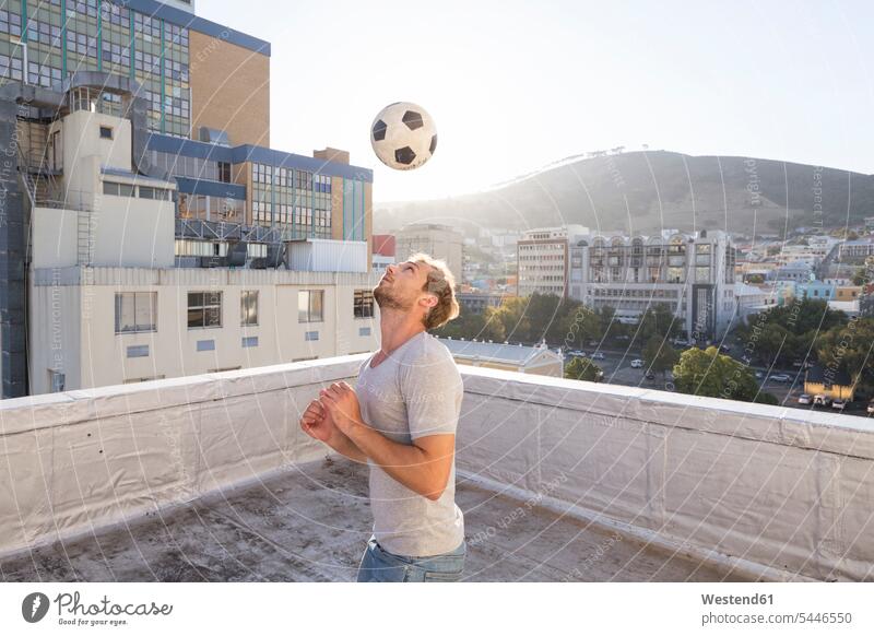 Young man playing football on rooftop terrace men males soccer parapet balustrade practicing practice practise exercise exercising practising blond blond hair