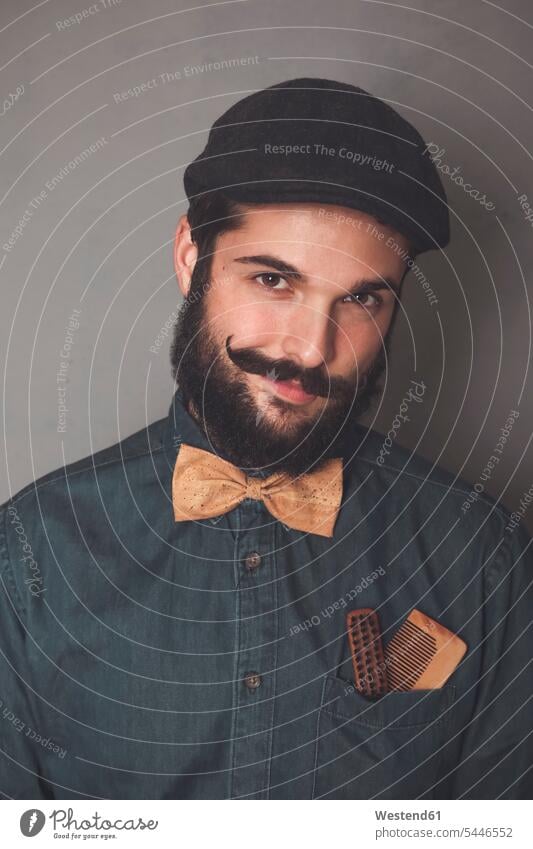 Portrait of bearded man wearing cap, denim shirt, cork bow tie, wearing wooden combs for beard and mustache in his pocket portrait portraits men males people