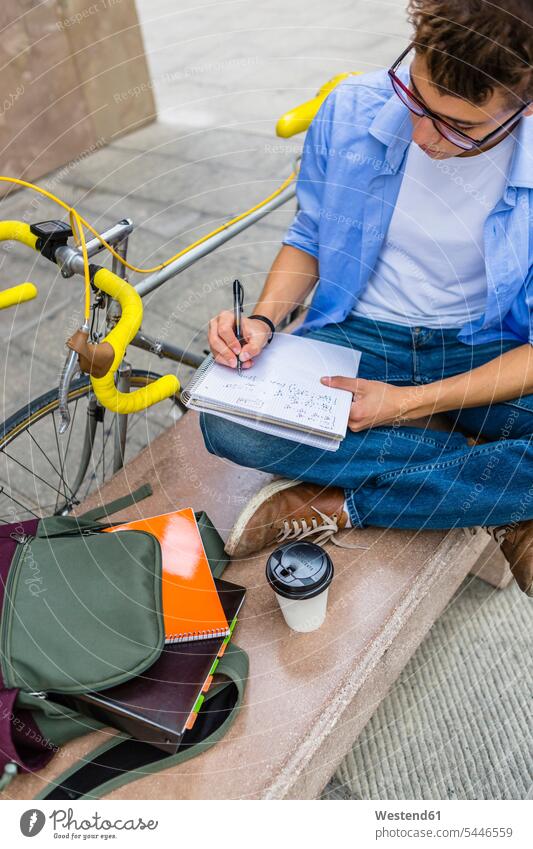 Young man with racing cycle sitting on bench writing on notepad student students write learning education bicycle bikes bicycles men males University Student