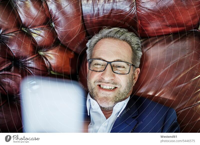 Smiling mature businessman lying down looking on cell phone laying down lie mobile phone mobiles mobile phones Cellphone cell phones smiling smile Businessman
