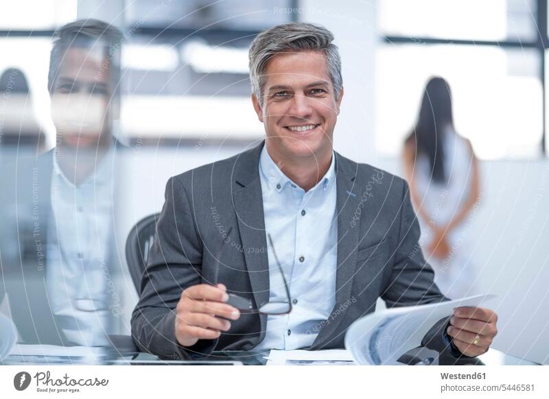 Businessman holding spectacles, reading documents Office Offices paper papers Business man Businessmen Business men friendly nice working At Work sitting Seated