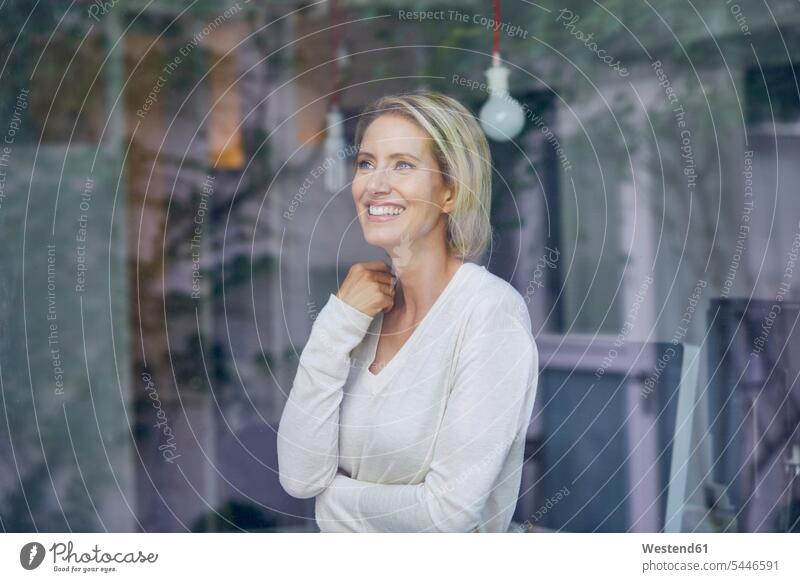 Portrait of laughing blond woman standing behind window pane portrait portraits females women Adults grown-ups grownups adult people persons human being humans