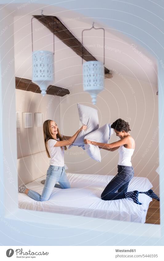 Playful female friends having a pillow fight in bed beds Fun having fun funny woman females women laughing Laughter Adults grown-ups grownups adult people