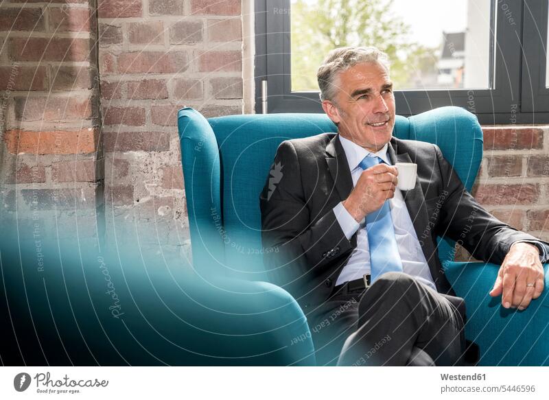 Mature businessman sitting in arm chair, drinking coffee Seated Success successful Coffee armchair Arm Chairs armchairs Taking a Break resting break Businessman