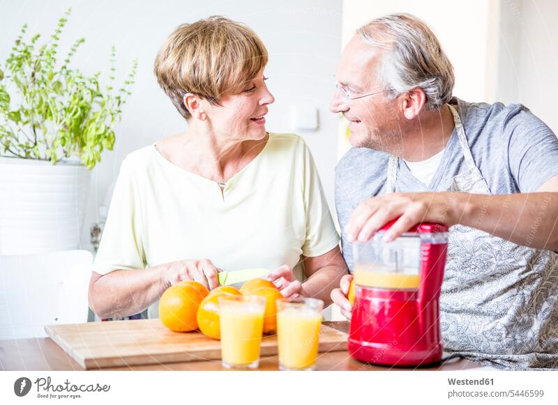 Senior couple in kitchen preparing freshly squeezed orange juice smiling smile Orange Juice twosomes partnership couples Fruit Juice Fruit Juices Drink