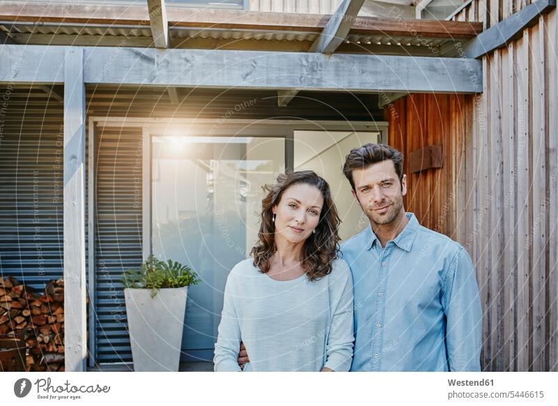 Couple standing in front of door of their home arm around arms around home ownership private owned home entrance entry Entryway entrances couple twosomes