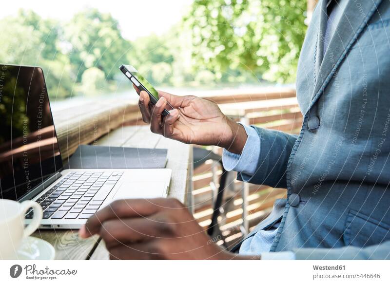 Businessman checking phone while working on his laptop on a terrace, partial view Smartphone iPhone Smartphones hand human hand hands human hands Business man
