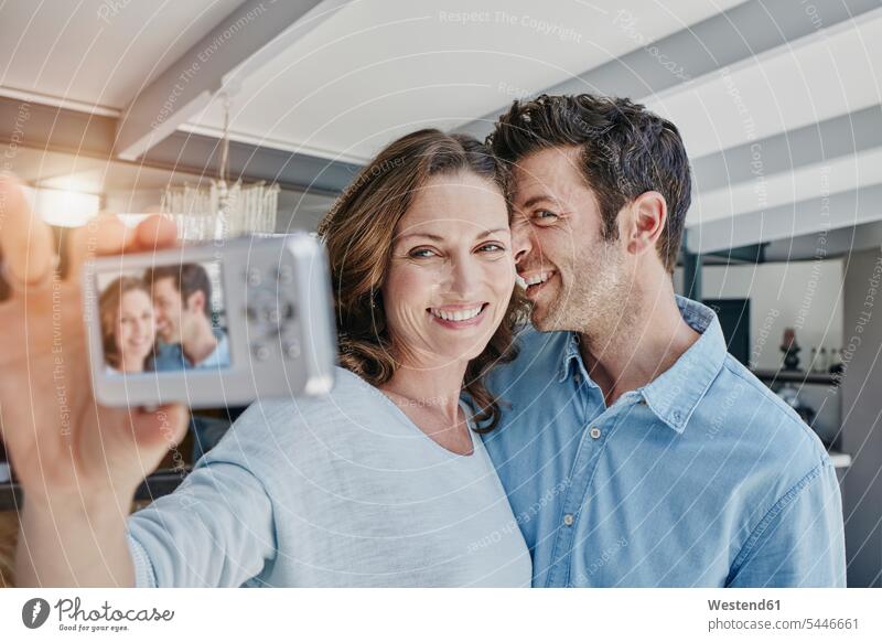 Happy couple taking pictures of themselves in their home Selfie Selfies twosomes partnership couples photographing taking a photo Taking Photos Taking A Picture