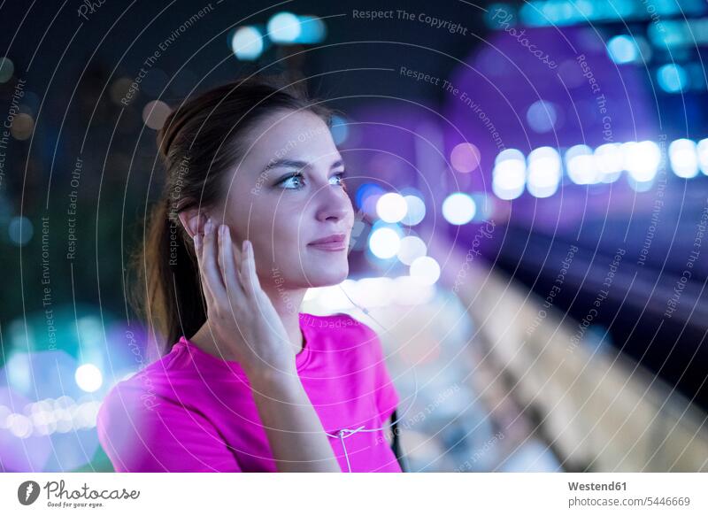Young woman in pink sportshirt listening to music in city at night young women young woman earphones ear phone ear phones Listening Music females Adults