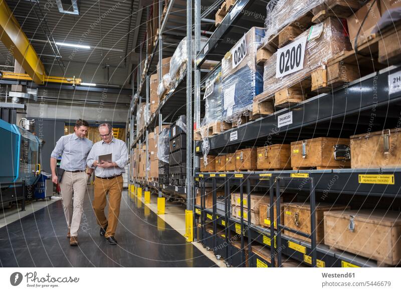 Two men with tablet walking in factory warehouse colleagues man males factories talking speaking Adults grown-ups grownups adult people persons human being