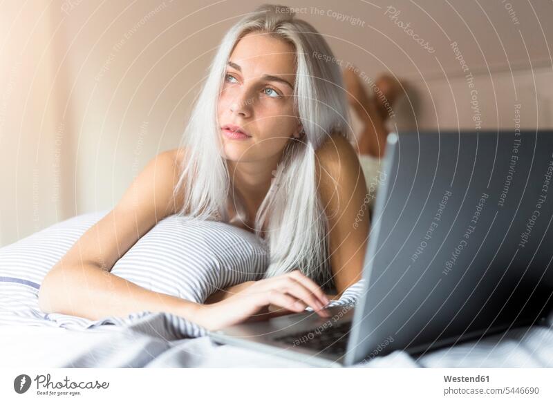 Young woman lying in bed using laptop laying down lie lying down Laptop Computers laptops notebook females women beds computer computers Adults grown-ups