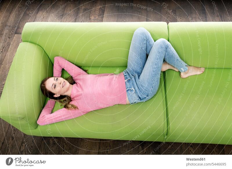Smiling young woman lying on the couch settee sofa sofas couches settees laying down lie lying down home at home females women smiling smile Adults grown-ups