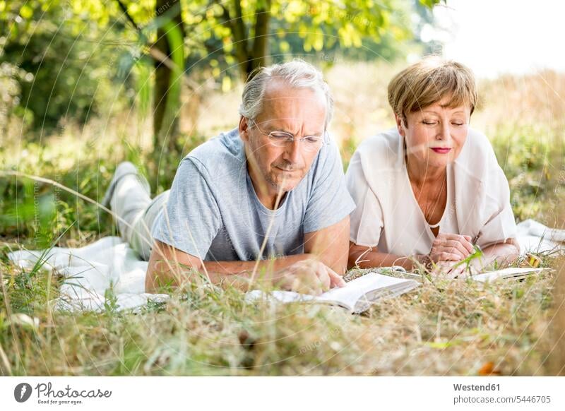 Senior couple lying in meadow reading a book meadows twosomes partnership couples relaxed relaxation books laying down lie lying down people persons human being