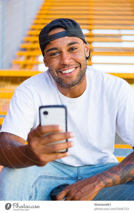 Portrait of smiling young man with smartphone sitting on stairs portrait portraits Smartphone iPhone Smartphones men males mobile phone mobiles mobile phones
