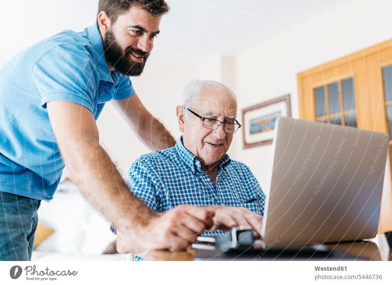 Adult grandson teaching his grandfather to use laptop grandpas granddads grandfathers grandsons senior men senior man elder man elder men senior citizen