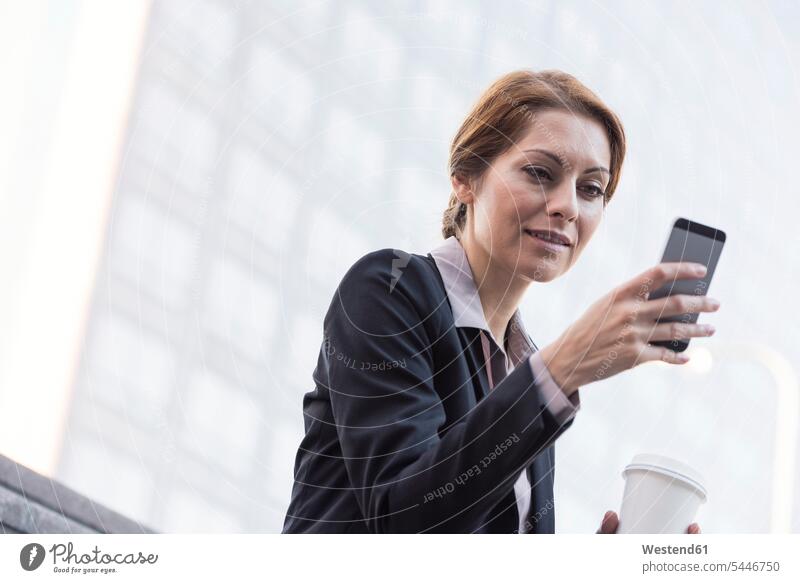 Smiling businesswoman holding cell phone and takeaway coffee businesswomen business woman business women business people businesspeople business world