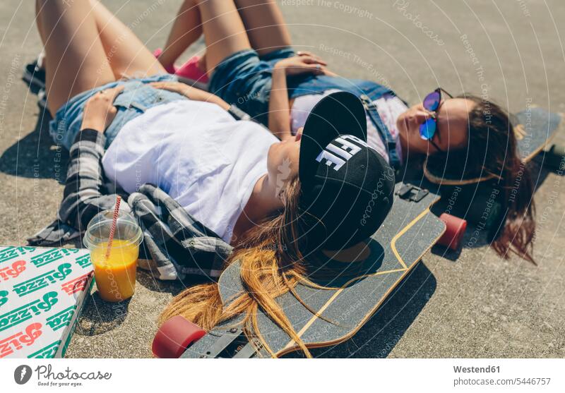 Two young women with longboards enjoying summer lying laying down lie lying down takeaway drink lying on back laying on back dorsal position summer time summery