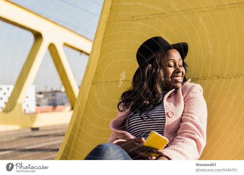 Young woman sitting on bridge using smartphone laughing Laughter relaxation relaxing Seated young bridges females women cheerful gaiety Joyous glad Cheerfulness
