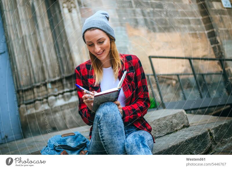 Spain, Barcelona, smiling young woman sitting on stairs writing in notebook females women notebooks Adults grown-ups grownups adult people persons human being