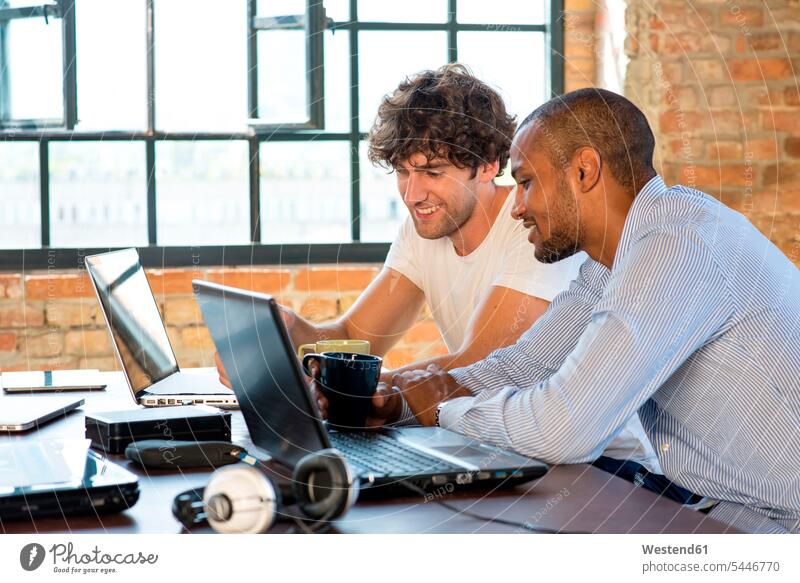 Two young businessmen working together in co-working space, using laptops colleagues Planning planning planned Coworking space shared workspace office sharing