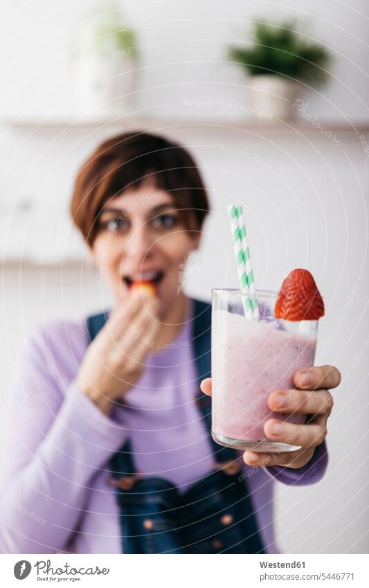 Woman holding glass of strawberry smoothie while eating a fruit Smoothies Drink beverages Drinks Beverage food and drink Nutrition Alimentation Food and Drinks