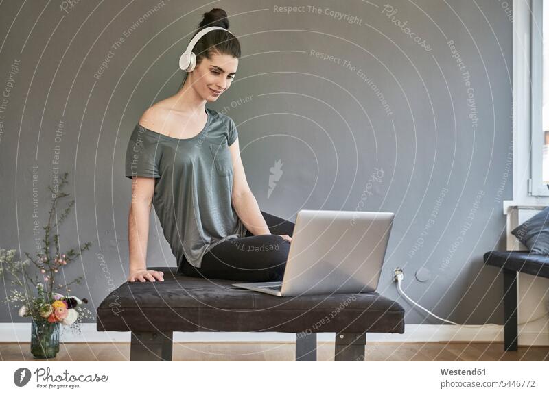 Young woman with headphones sitting on lounge using laptop females women Laptop Computers laptops notebook headset Adults grown-ups grownups adult people