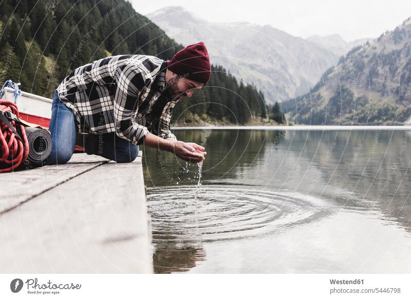 Austria, Tyrol, Alps, man kneeling on jetty scooping water from mountain lake jetties men males lakes Adults grown-ups grownups adult people persons human being