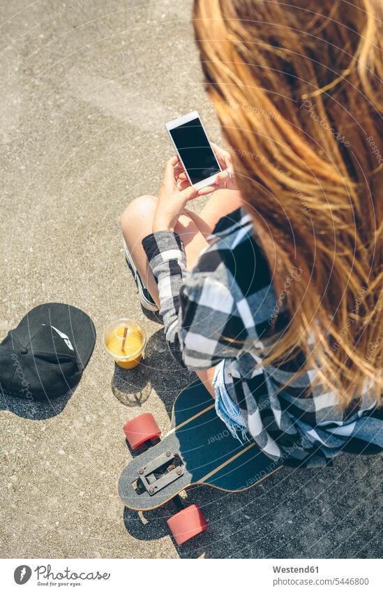 Back view of young woman with long hair looking sitting on longboard looking at smartphone females women Adults grown-ups grownups adult people persons