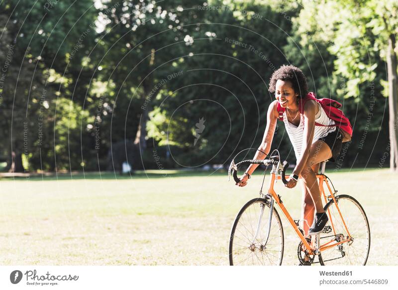 Smiling young woman riding bicycle in park bikes bicycles females women parks smiling smile driving drive Adults grown-ups grownups adult people persons