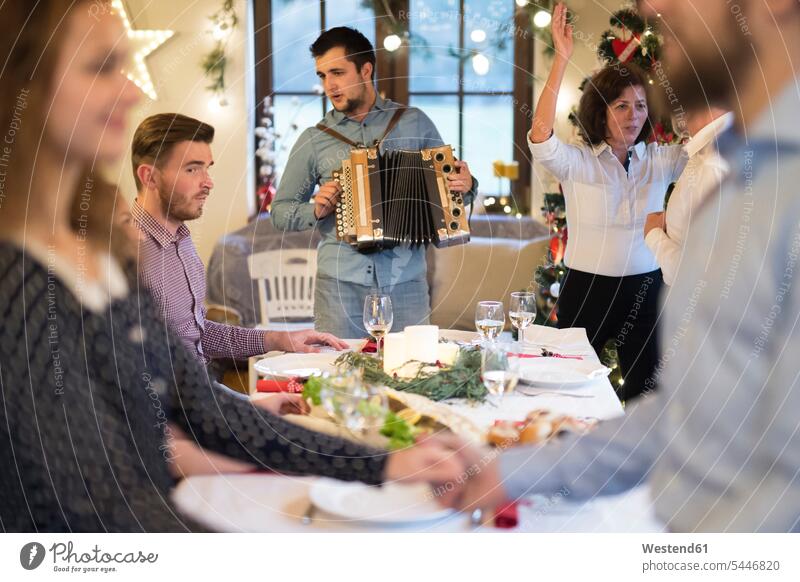 Young man playing accordion for family at Christmas accordions X-Mas yule Xmas X mas families celebrating celebrate partying keyboard instrument