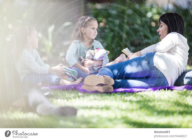 Mother reading a book to children on picnic blanket family families Picnic picnicking mother mommy mothers ma mummy mama books daughter daughters girl females