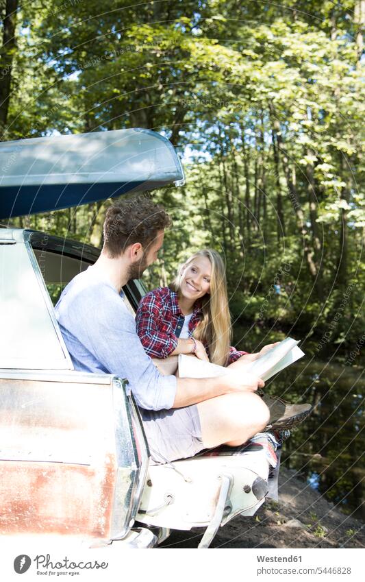 Smiling young couple with map and canoe in car at a brook maps brooks rivulet twosomes partnership couples forest woods forests smiling smile automobile Auto