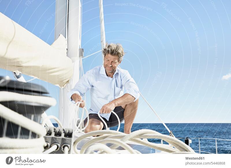 Mature man working with ropes on sailing boat men males Adults grown-ups grownups adult people persons human being humans human beings boat sports At Work