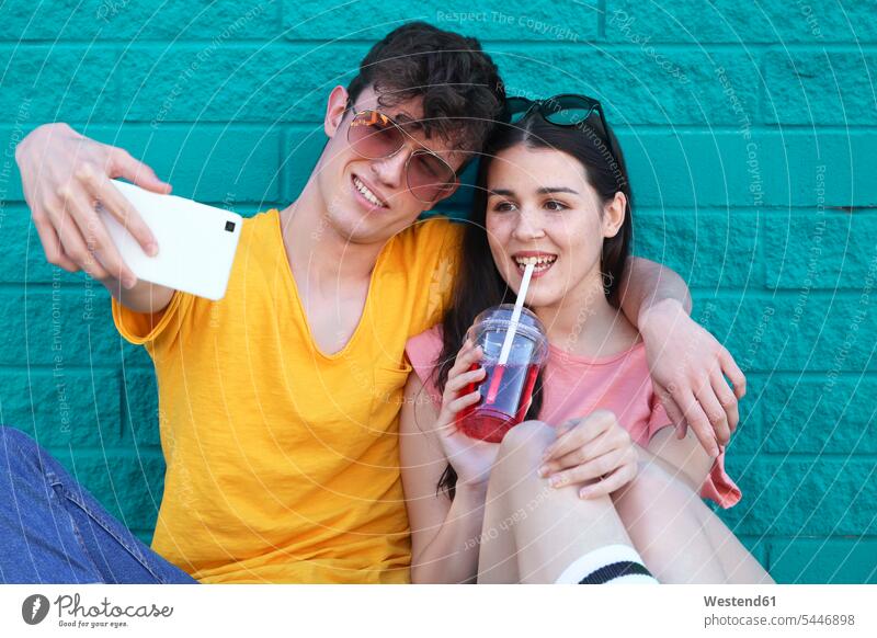 Young couple taking selfie with smartphone in front of blue brick wall Selfie Selfies twosomes partnership couples portrait portraits people persons human being