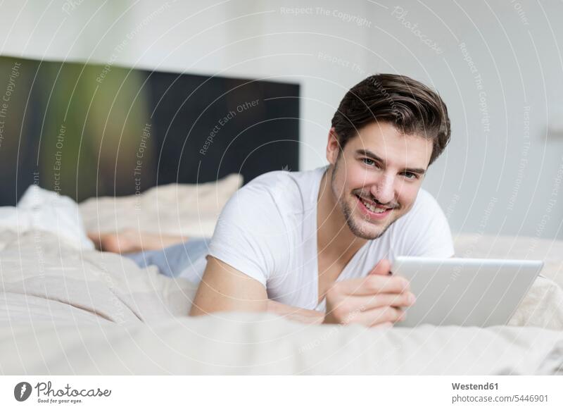 Portrait of smiling man lying on bed using tablet smile men males beds Adults grown-ups grownups adult people persons human being humans human beings front view