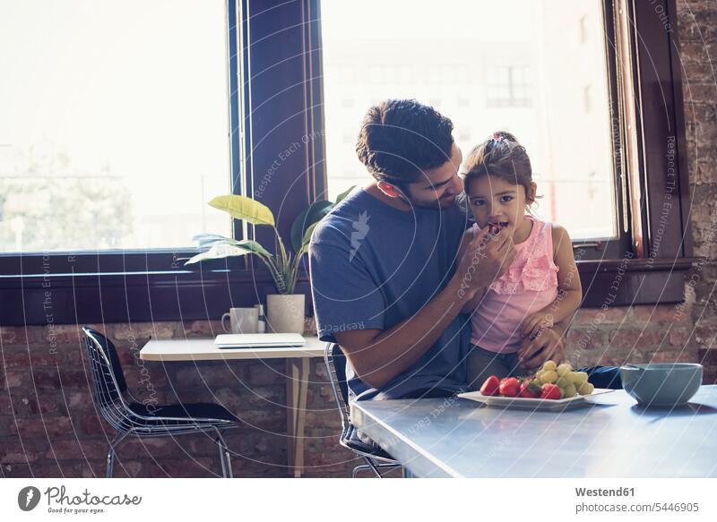 Father feeding daughter in kitchen eating daughters father pa fathers daddy dads papa home at home Fruit Fruits child children family families people persons