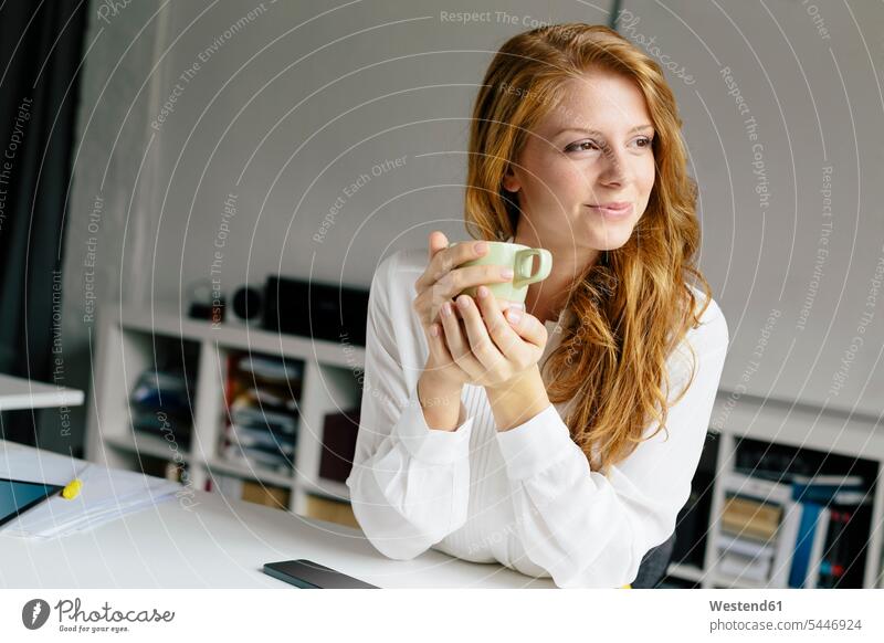 Smiling young woman with cup of coffee at desk in office smiling smile confidence confident females women offices office room office rooms Coffee Coffee Cup