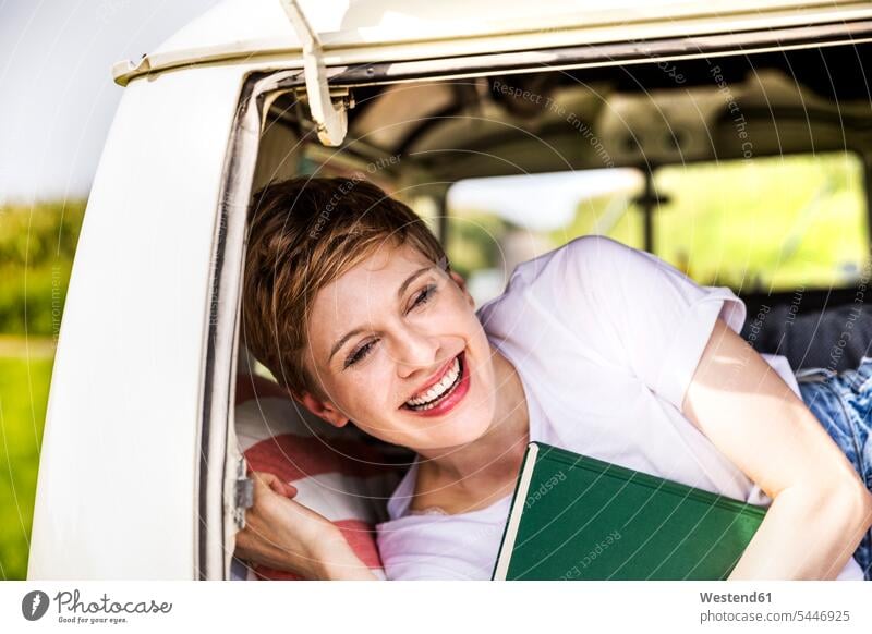 Happy woman with book in a van laughing Laughter females women books positive Emotion Feeling Feelings Sentiments Emotions emotional motor vehicle road vehicle