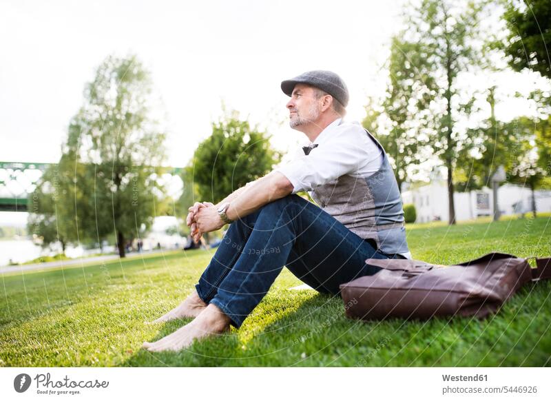 Mature businessman in the city park sitting on grass relaxed relaxation men males Seated break meadow meadows relaxing Adults grown-ups grownups adult people