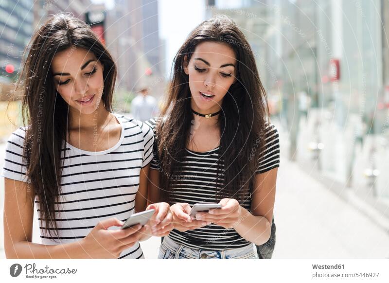 USA, New York City, two twin sisters looking at cell phones in Manhattan mobile phone mobiles mobile phones Cellphone female friends New York State telephones