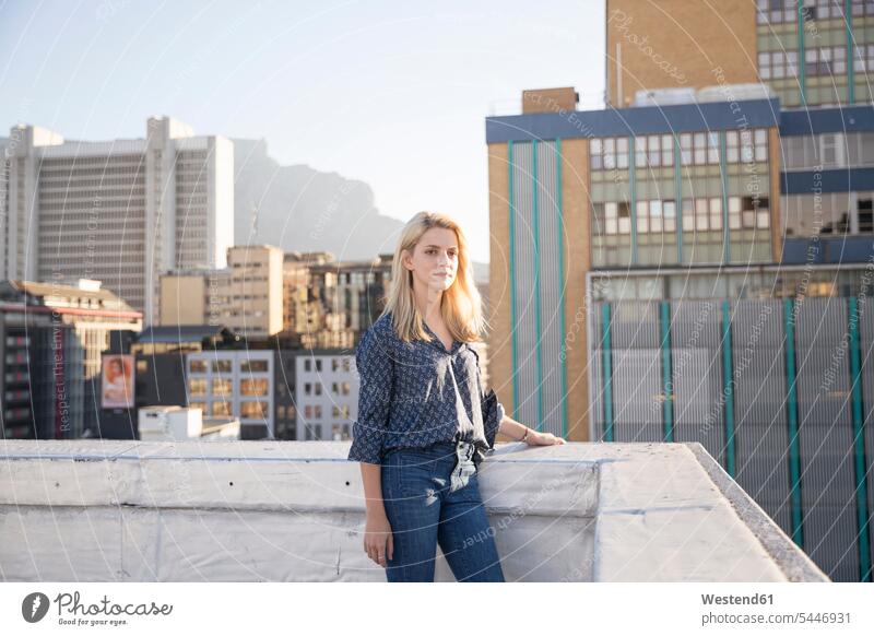 Young woman standing on a rooftop terrace females women serious earnest Seriousness austere parapet balustrade blond blond hair blonde hair roof terrace deck