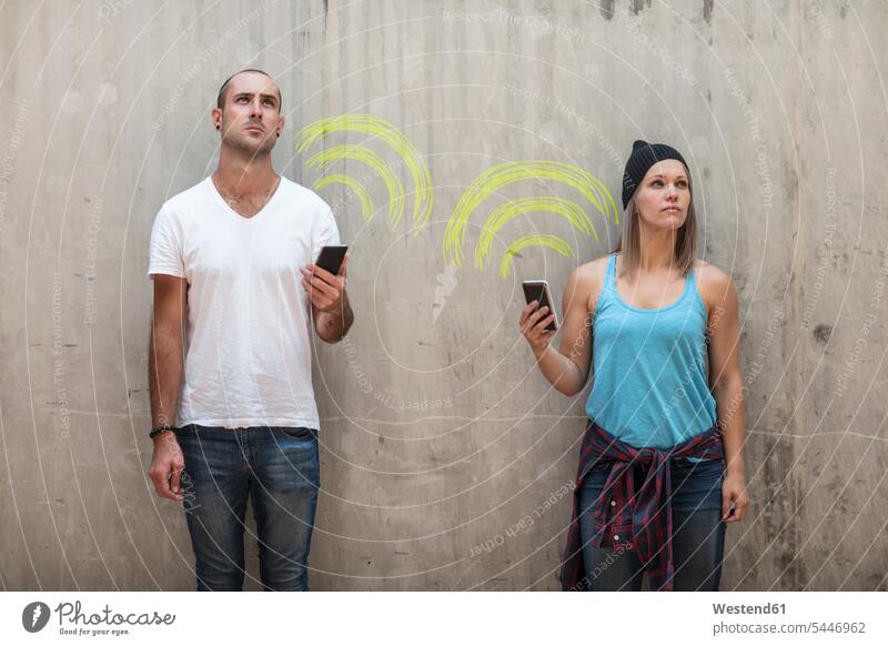 Man and woman holding their phones with wifi sign in chalk wall walls symbol symbols Wifi Wi-Fi wireless internet WLan wireless lan W-Lan mobile phone mobiles