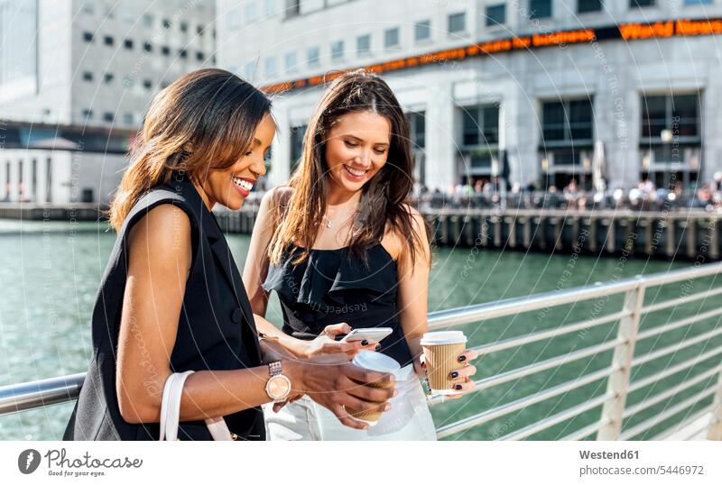 Two women on a bridge with takeaway coffee and cell phone Coffee smiling smile Female Colleague mobile phone mobiles mobile phones Cellphone cell phones woman