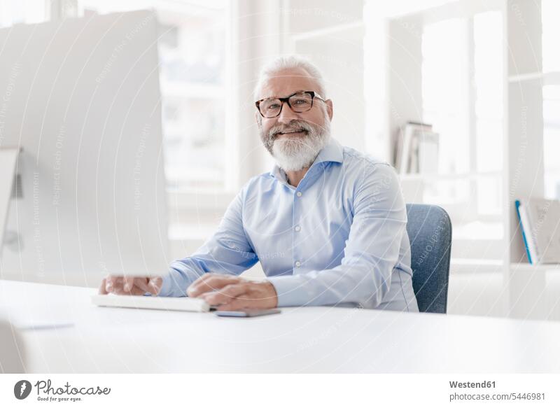 Smiling mature man with beard and glasses at desk men males portrait portraits smiling smile Adults grown-ups grownups adult people persons human being humans