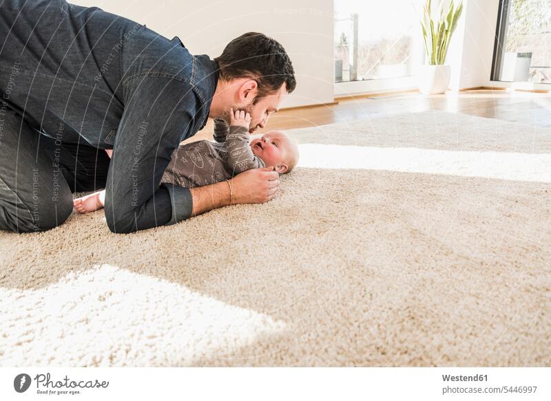 Father and baby son playing on carpet at home father pa fathers daddy dads papa hugging cuddling laughing Laughter babies infants parents family families people