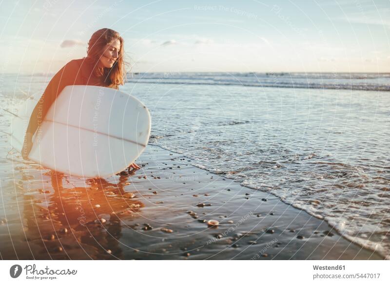 Young woman with surfboard crouching at seashore surfboards surfer female surfer surfers female surfers surfing surf ride surf riding Surfboarding water sports